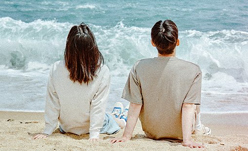 해변 모래사장에 나란히 앉은 남녀의 뒷모습